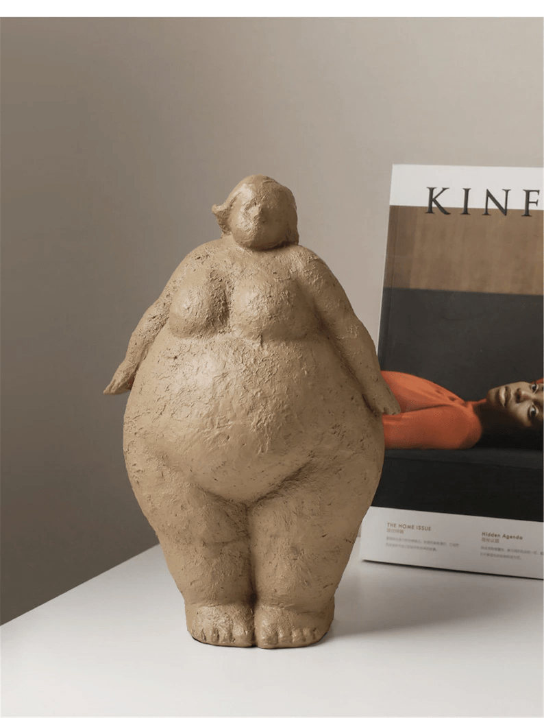 A textured brown ceramic sculpture of a plump, standing figure, beside a magazine titled "KIN".